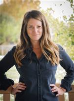 Nancy Hobbin standing outside by trees wearing a blue button up shirt 